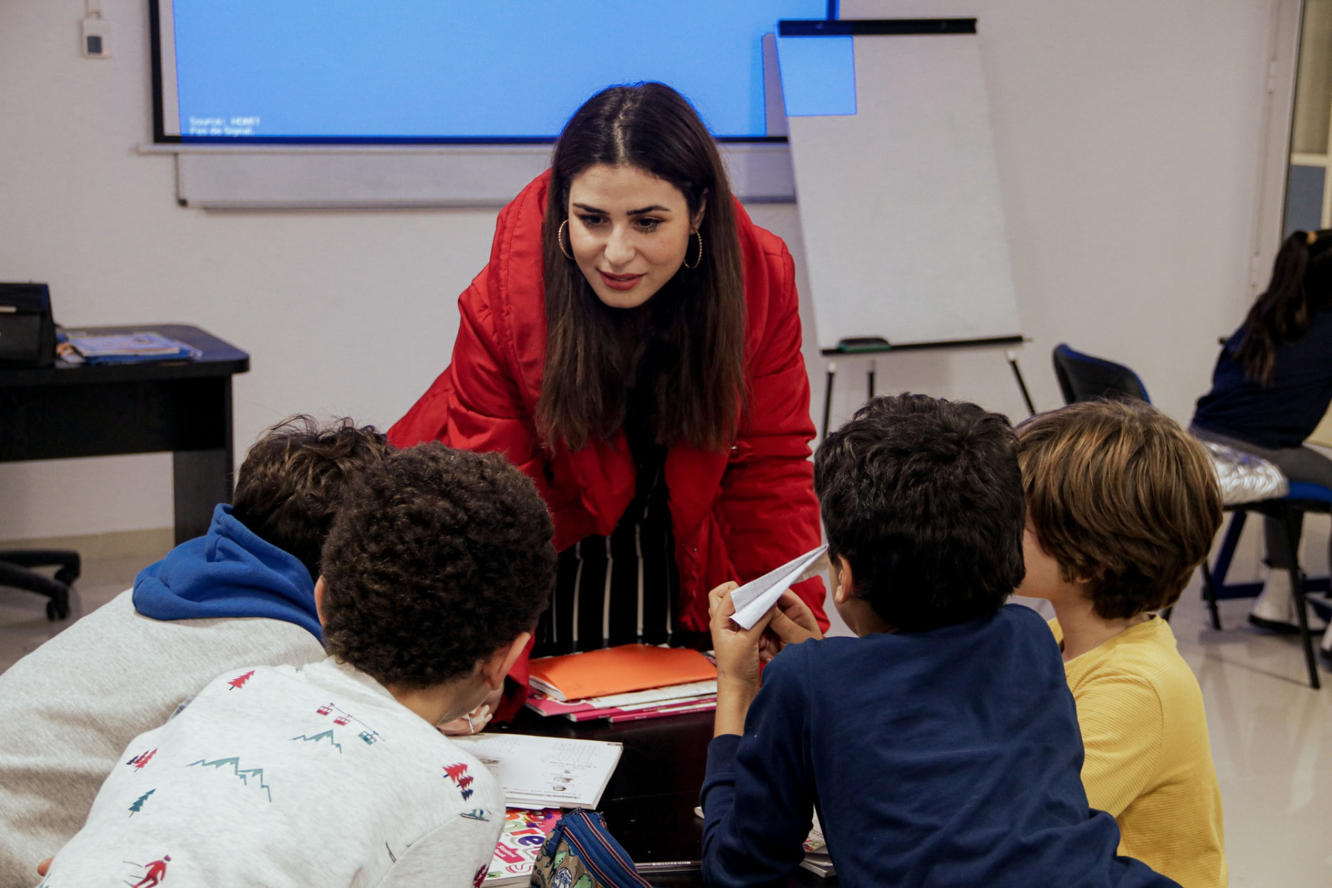 An instructor in a red jacket leaning over a table to work with four children