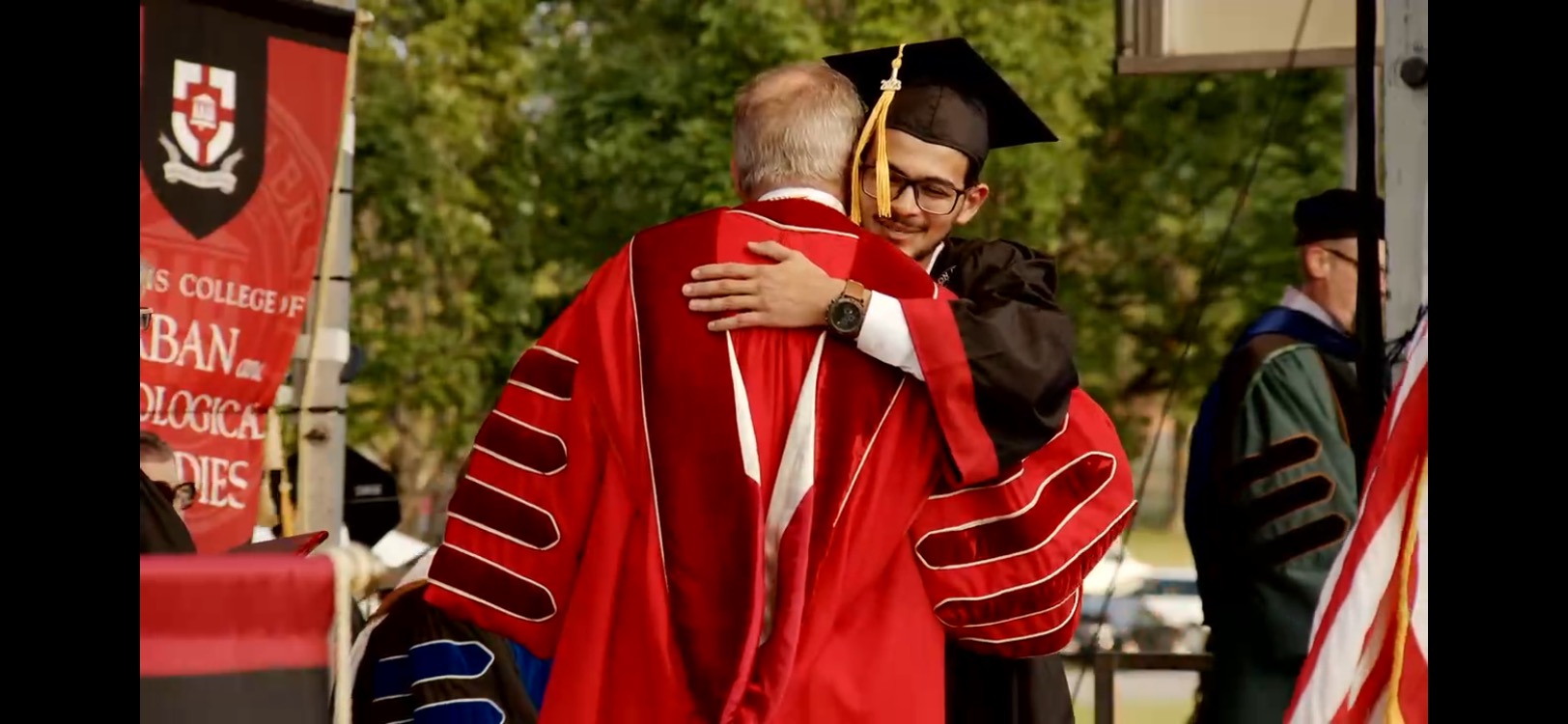 A graduate embracing a university official on the commencement stage