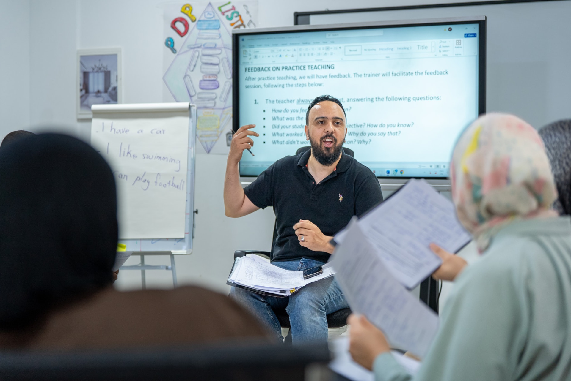 A teacher trainer presenting in front of a screen reading Feedback on Practice Teaching