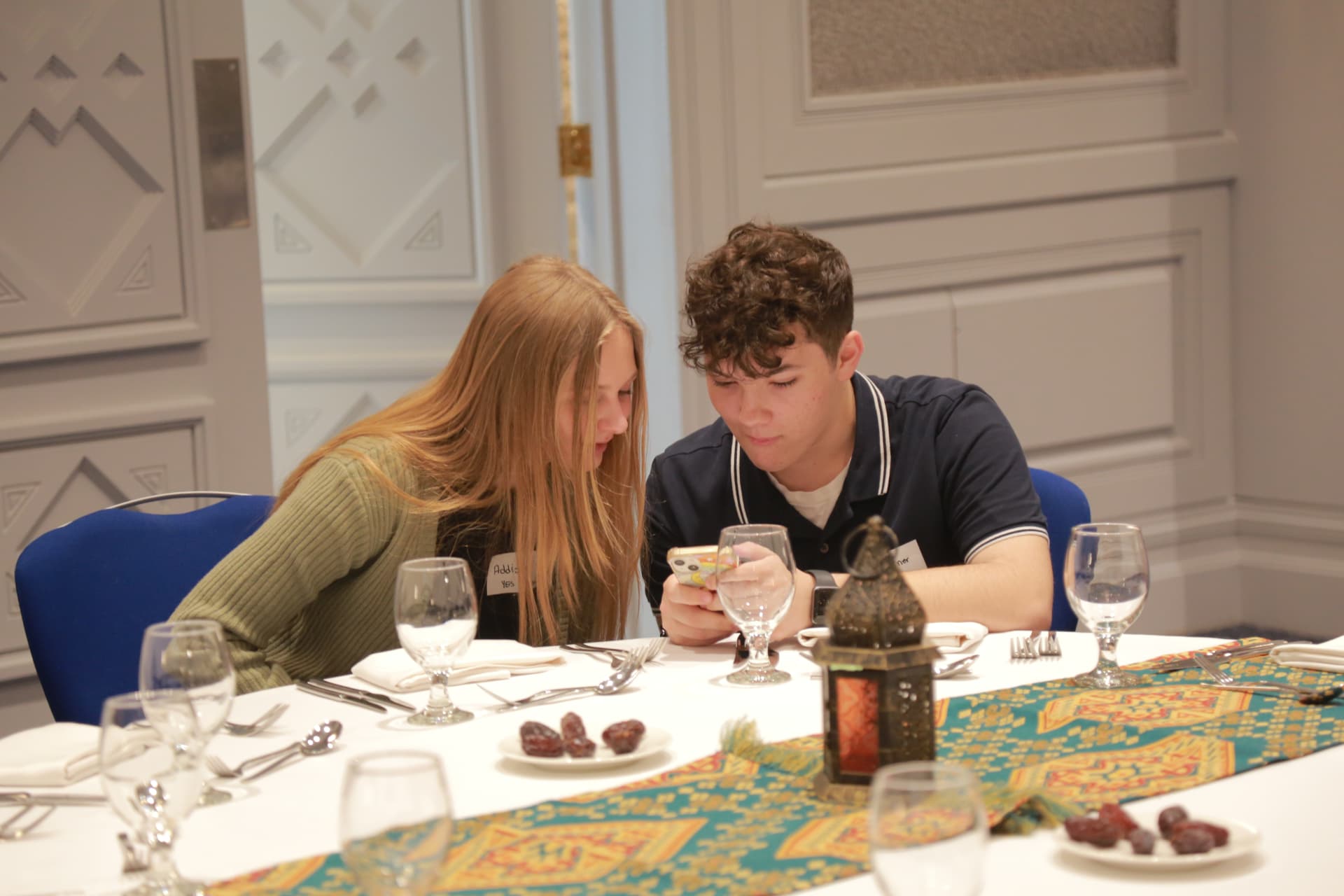 Two young people looking at a smartphone together at a formal dinner table