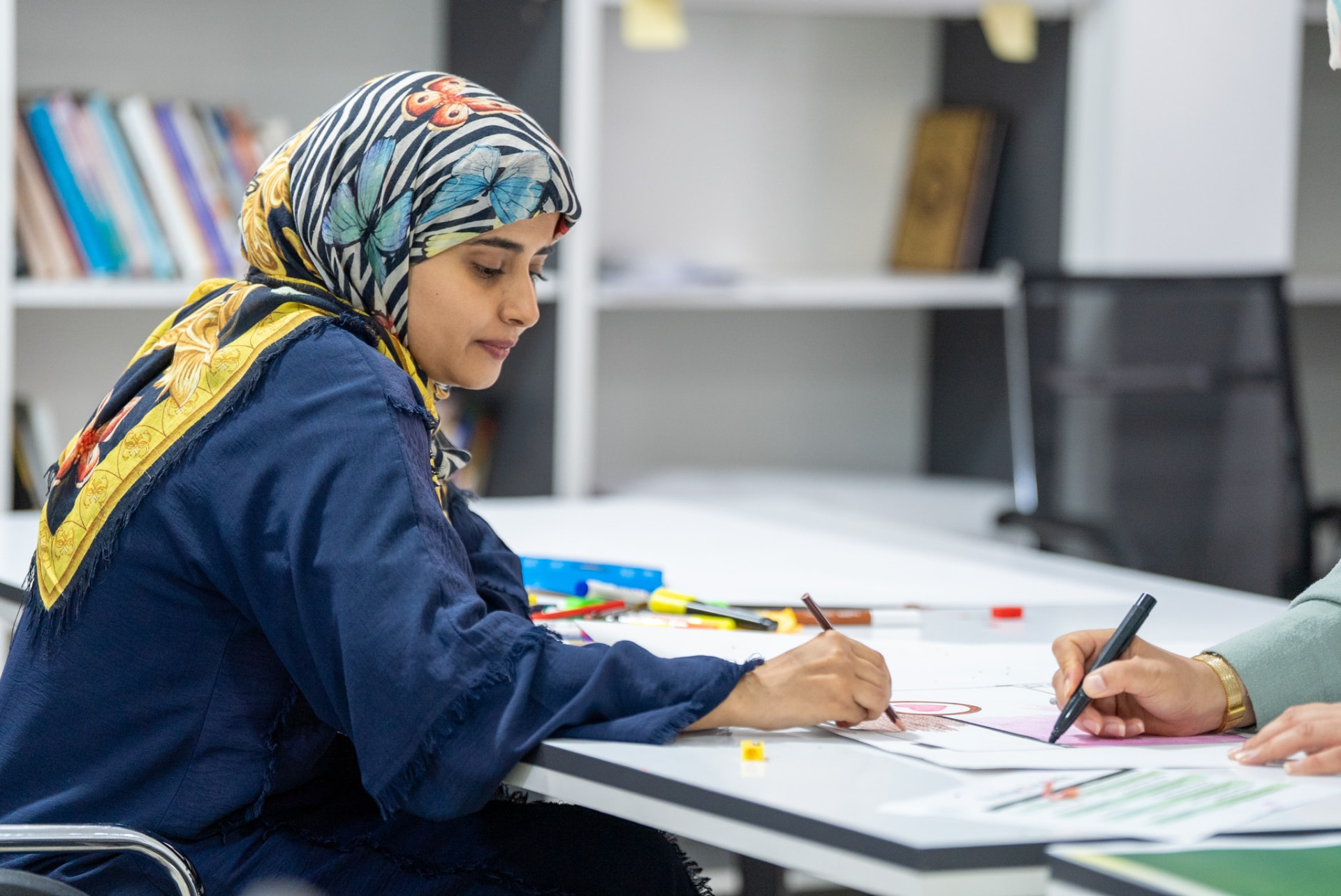 A woman in a patterned headscarf drawing on a large sheet of paper during a workshop