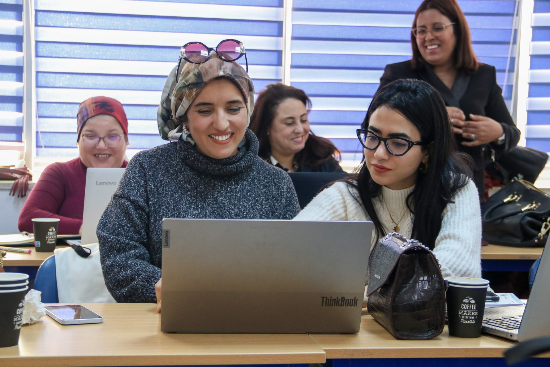 Two women smiling as they look at a laptop together in a classroom in Tunisia