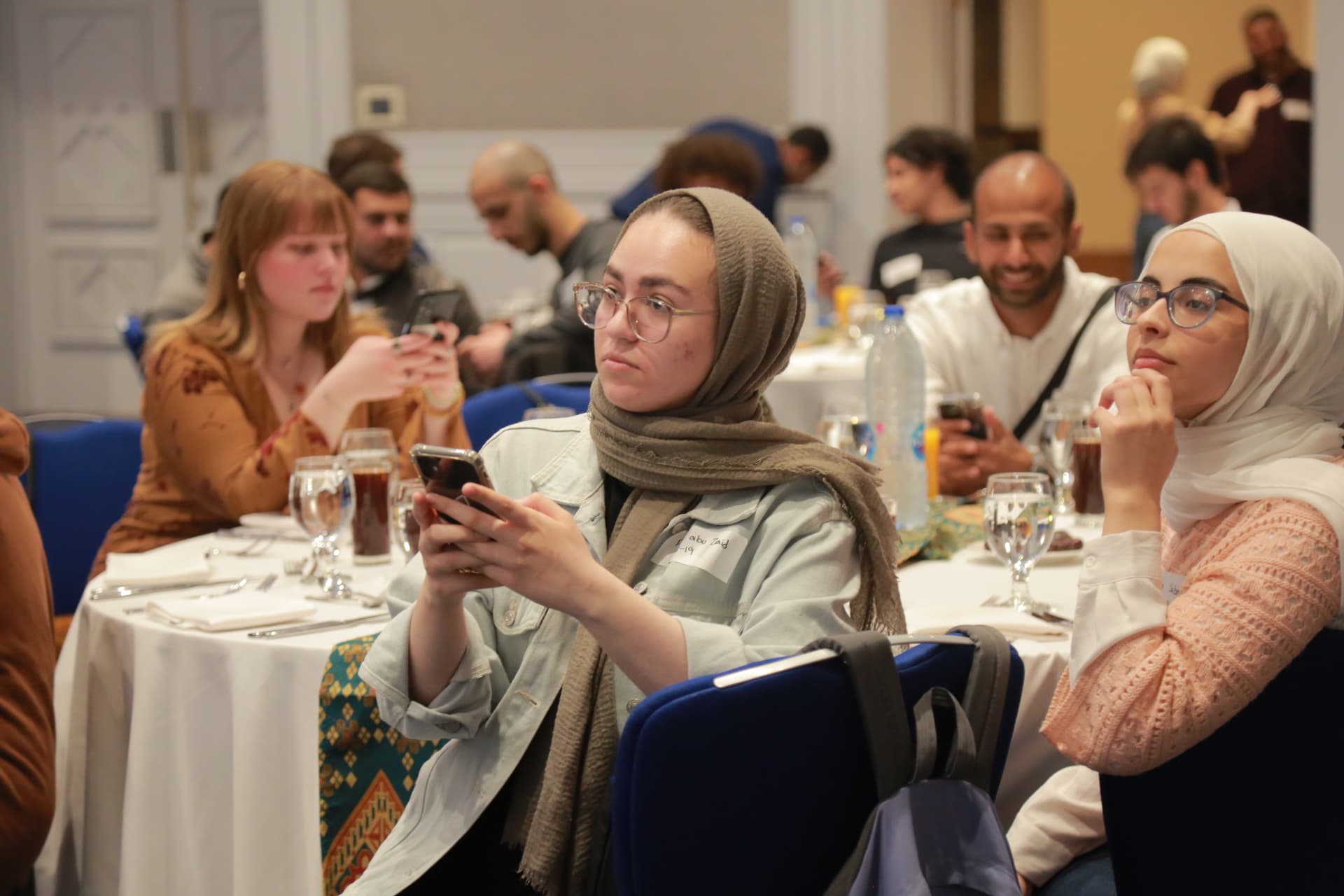 Young adults seated at tables in a brightly lit event hall