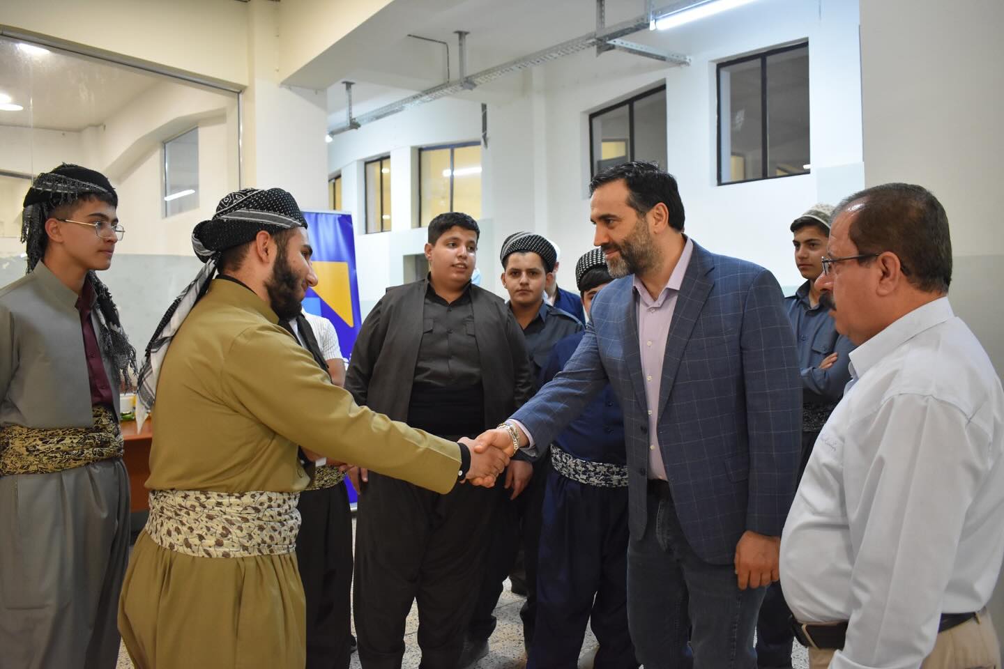 An instructor shaking hands with a student in traditional Kurdish dress, surrounded by classmates