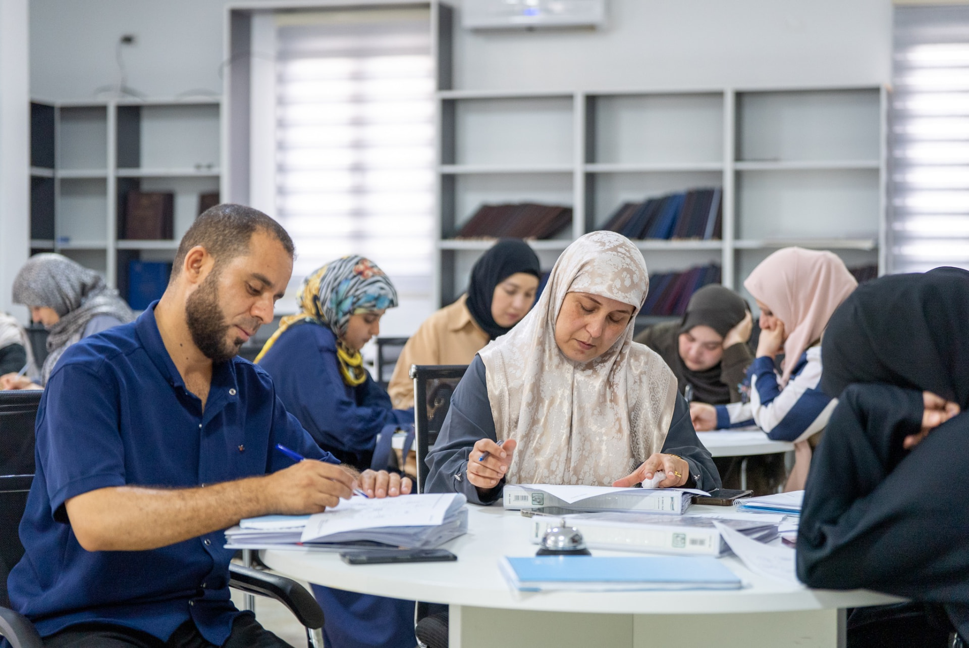 A man and a woman seated at a classroom table in Libya working through their workbooks