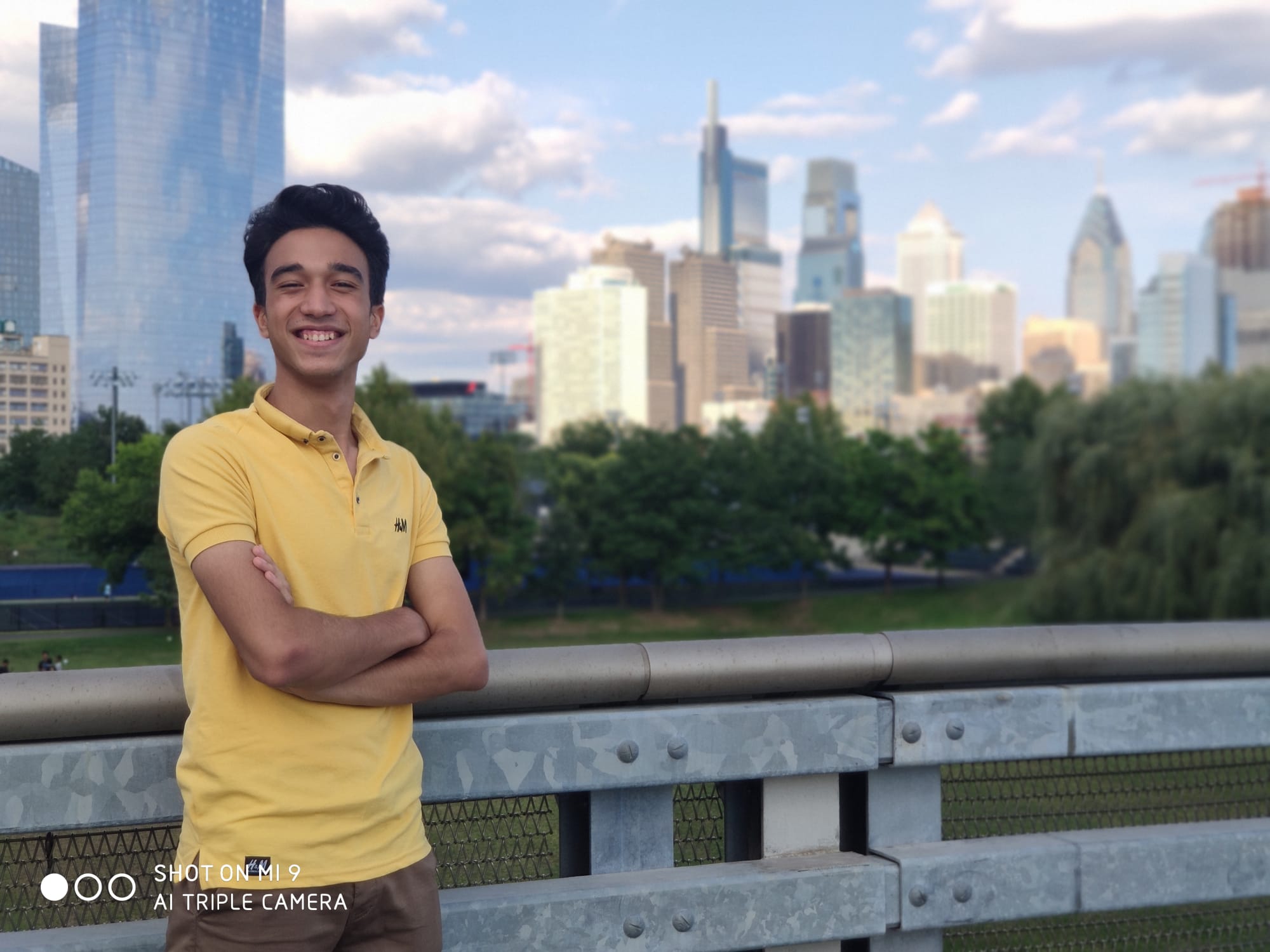 A young man standing with arms crossed, a city skyline behind him
