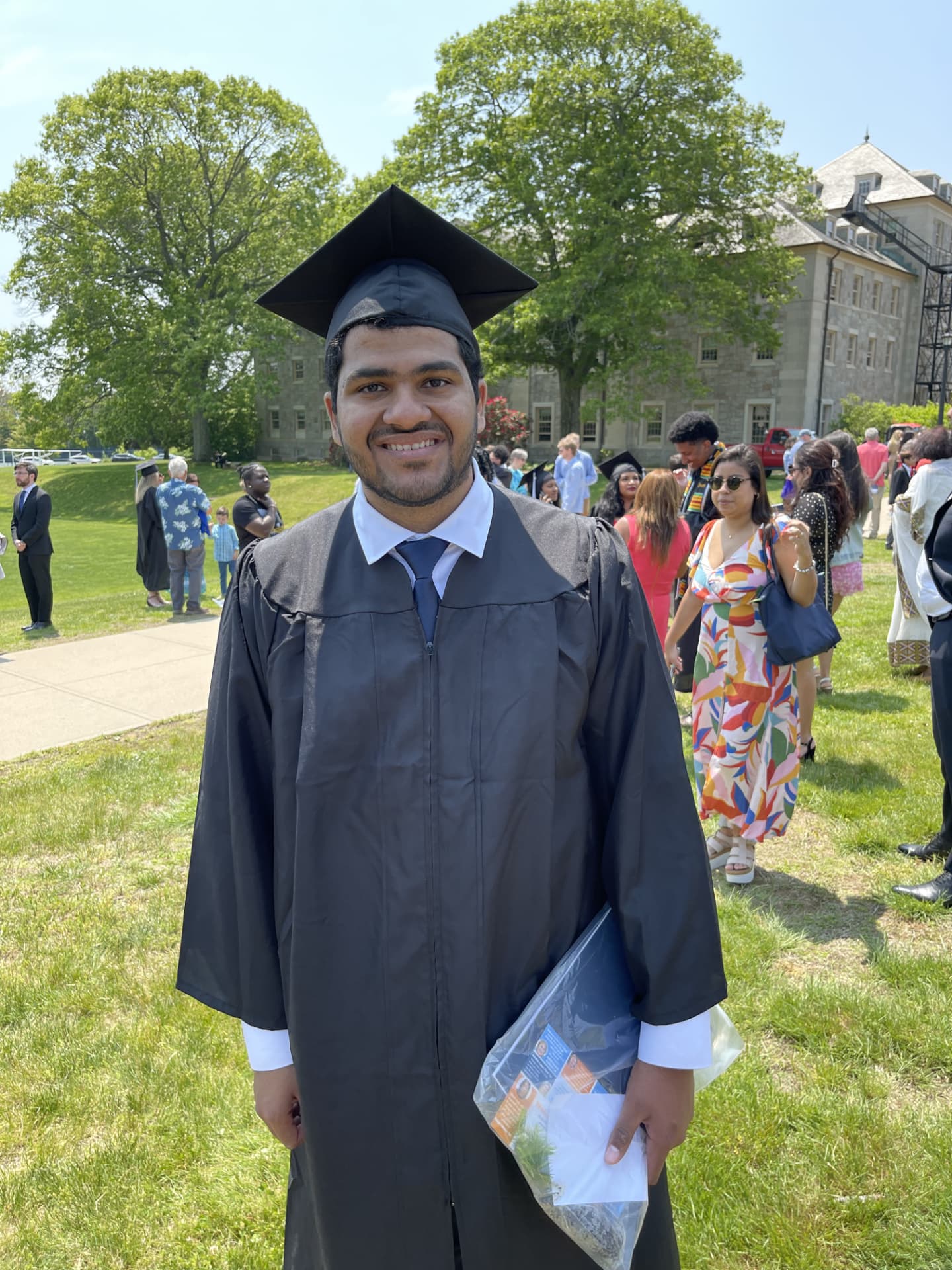 A smiling graduate in cap and gown at an outdoor commencement ceremony